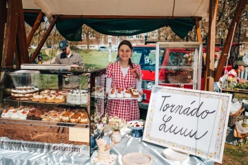 Žena v zástěře ve stánku Tornádo Lulu v červenobílé kostkované košili nabízí dezerty na festivalu.