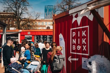 Návštěvníci festivalu míří k červenému stánku PIKNIK BOX mezi ostatními stánky.
