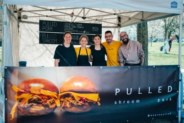 Tým prodejců u stánku s burgery Pulled pózuje před nabídkou jídel.