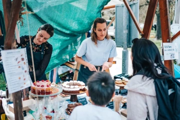 Ženy za stánkem s pečenými dorty a zákusky obsluhují návštěvníky festivalu.