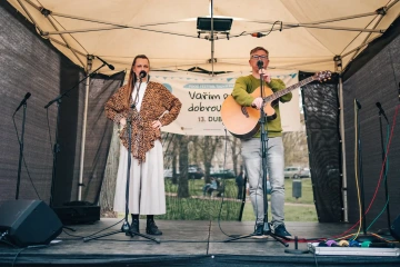 Dvě zpěvačky a kytarista vystupují na pódiu festivalu před bannery s logem akce.