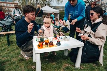 Rodiny s dětmi u nízkého stolečku s barvami, děti se věnují malování na festivalu.
