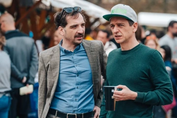 Dva muži v ležérním oblečení diskutují mezi návštěvníky na venkovní části festivalu.