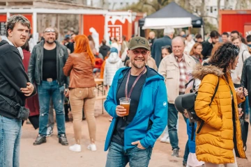 Návštěvníci festivalu se procházejí mezi stánky, někteří drží v ruce občerstvení nebo nápoje.