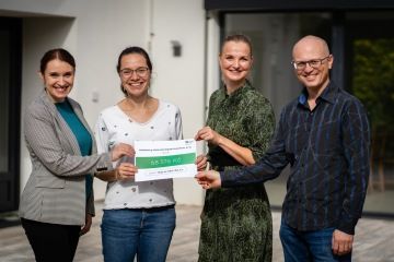 Skupiny lidí, která pózuje se šekem, představujícím finanční podporu pro Nový domov.